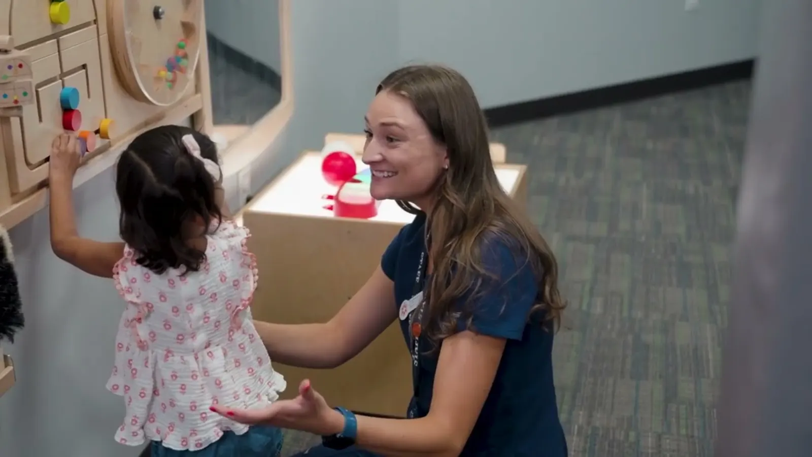 A Brighton Center therapist playing with a toddler at a sensory wall